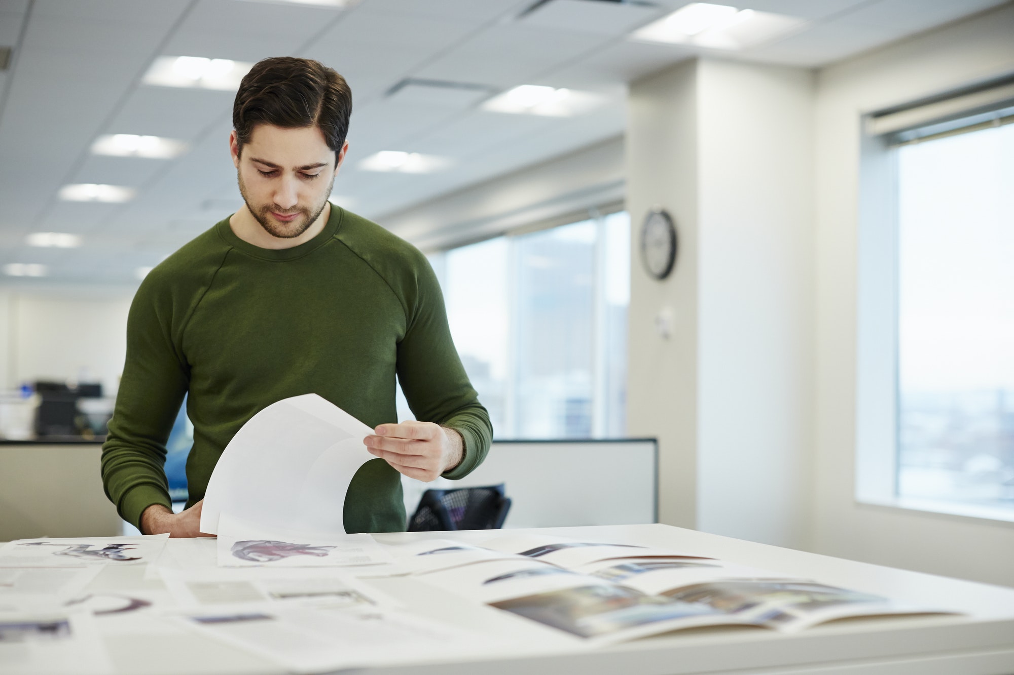 A man in an office checking proofs of printed pages.