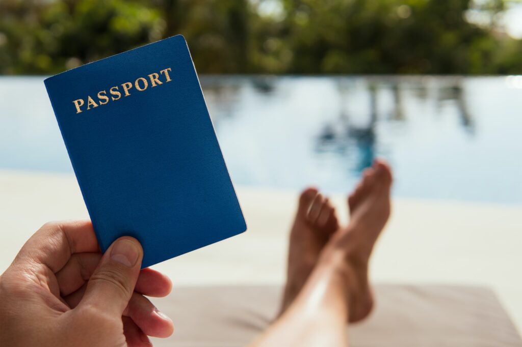 Man Holds A Passport In His Hand On The Tropical Background